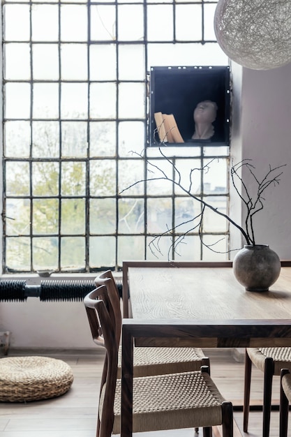 Stylish composition of modern dining room interior design with wooden table and chairs and accessories. Spacious room with creative walls and parquet floor.