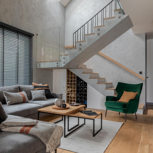 Stylish composition of modern living room design with corner grey sofa green armchair coffee table and minimalist personal accessories Stairs in living room interior Concrete walls Template