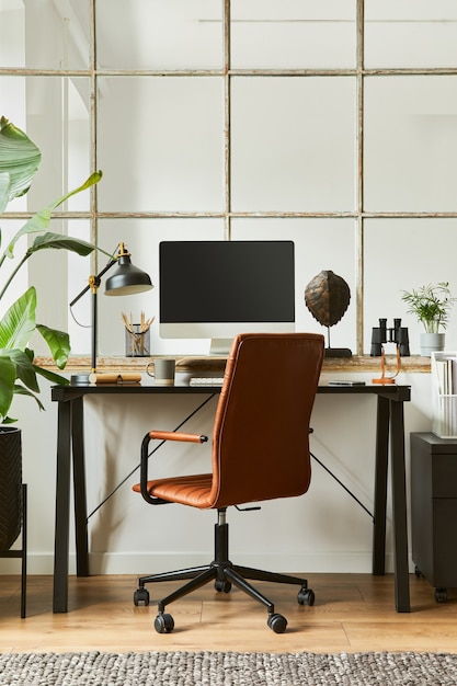 Elegante composizione del moderno design d'interni per l'area di lavoro dell'ufficio domestico maschile con scrivania industriale nera, poltrona in pelle marrone, pc e accessori personali eleganti. modello.