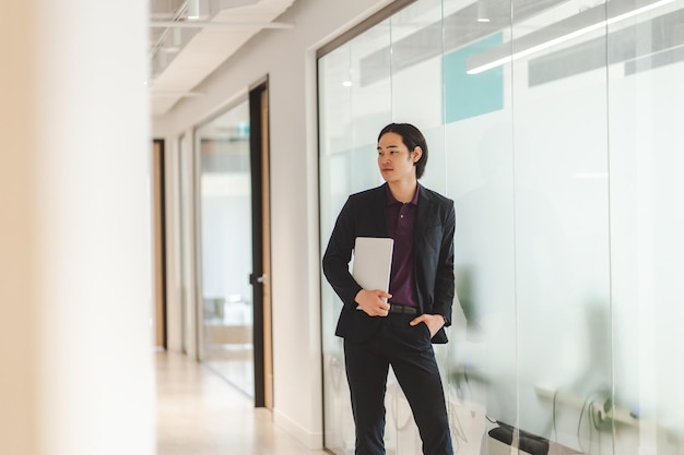 stylish confident Asian businessman wearing formal wear black suit holding laptop looking away