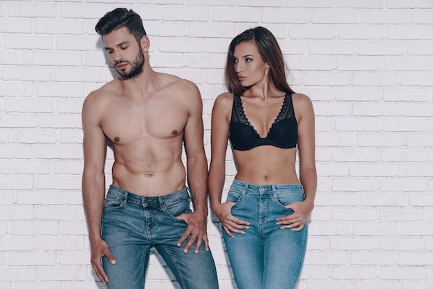 Photo stylish couple. beautiful young couple looking away while standing against brick wall