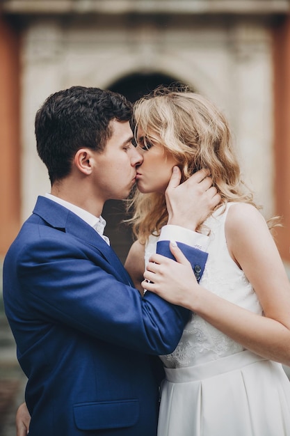 Стильная пара обнимается и целуется на улице европейского города Чувственный страстный момент Модная влюбленная невеста и жених нежно обнимаются в День святого Валентина
