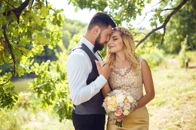 Stylish couple of happy newlyweds posing in the park on their wedding day