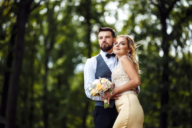 Stylish couple of happy newlyweds posing in park on wedding day. Perfect couple bride groom posing