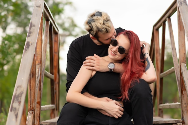 Elegante coppia innamorata in abiti neri stanno camminando nel parco e abbracciando una coppia adorabile di hipster sorridendo e godendosi il tempo insieme concetto di amore e stile di vita giovanile