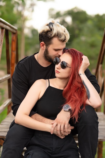 Stylish couple in love in black clothes are walking in the park and hugging Lovely hipster couple smiling and enjoying time together Youth love and lifestyle concept