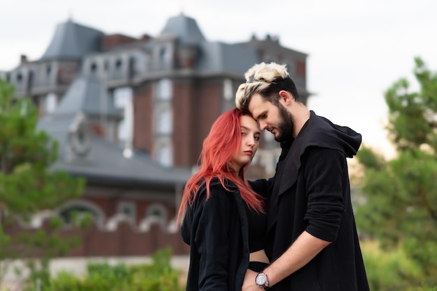 Stylish couple in love in black clothes walks in the park and hugs Lovely couple of hipsters hugging on the background of the house Youth love and lifestyle concept