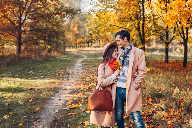 Stylish couple in love walks in autumn park among colorful trees. Happy man and woman hugging outdoors at sunset