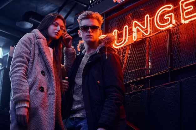 Stylish couple wearing warm clothes standing in the cafe with industrial interior, a backlit signboard in the background