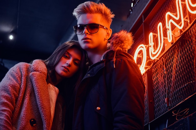 Stylish couple wearing warm clothes standing in the cafe with industrial interior, a backlit signboard in the background