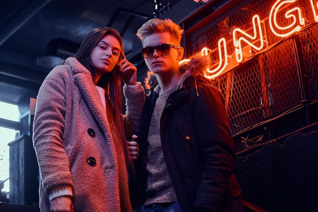 Stylish couple wearing warm clothes standing in the cafe with industrial interior, a backlit signboard in the background