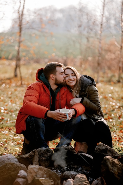 Photo stylish couple with cup of coffee near bonfire