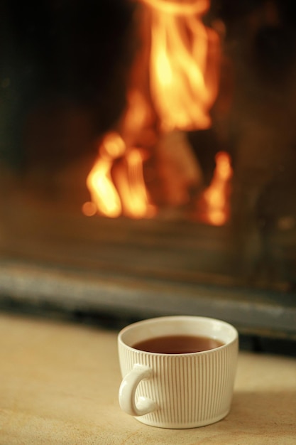 사진 타는 벽난로를 배경으로 따뜻한 차 한 잔이 가을 겨울 휘게를 닫습니다.
