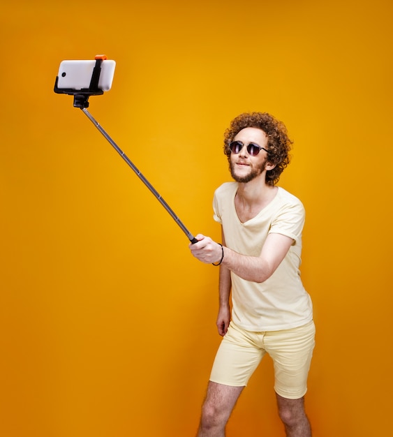 Photo stylish curly-haired man taking selfie with monopod