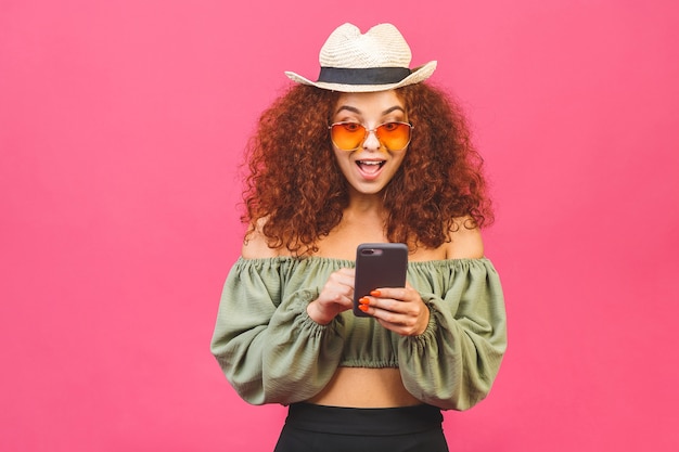 Stylish curly young girl or woman in a straw hat with sunglasses isolated over pink background