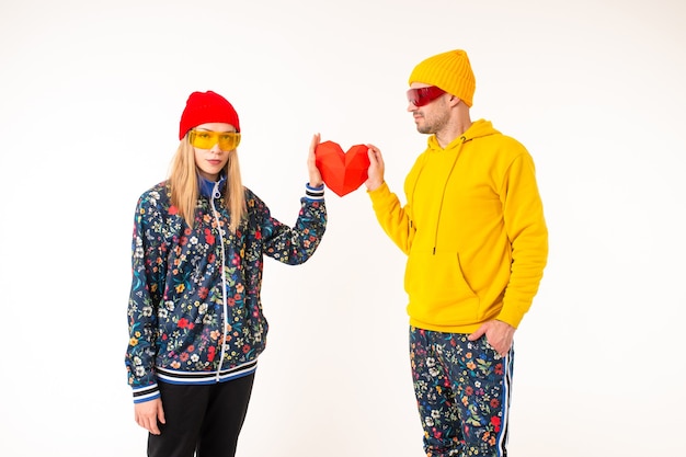 Stylish cute couple of man and woman in colorful clothes holding heart over white wall