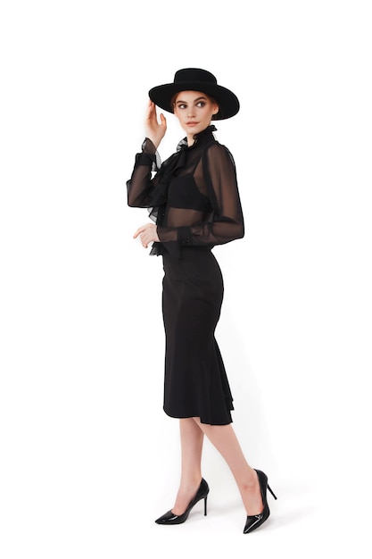 Stylish cute young businesswoman in black elegant blouse and hat on white isolated wall. Woman in fashionable clothes posing. Concept of style, fashion,