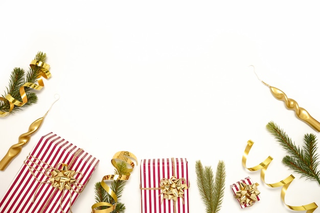 Stylish decor concept, christmas red striped gift box, golden ribbons, bow, candles, fir branches on white backdrop.