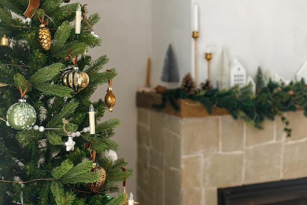 Stylish decorated christmas tree with vintage baubles and modern decor on fireplace mantel with bells and ribbon Modern christmas scandinavian living room Atmospheric christmas eve