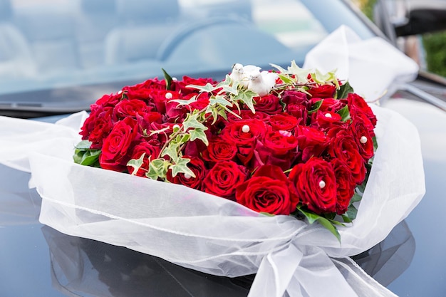 A stylish decoration of red rose flowers, ribbons on a shiny
black wedding car