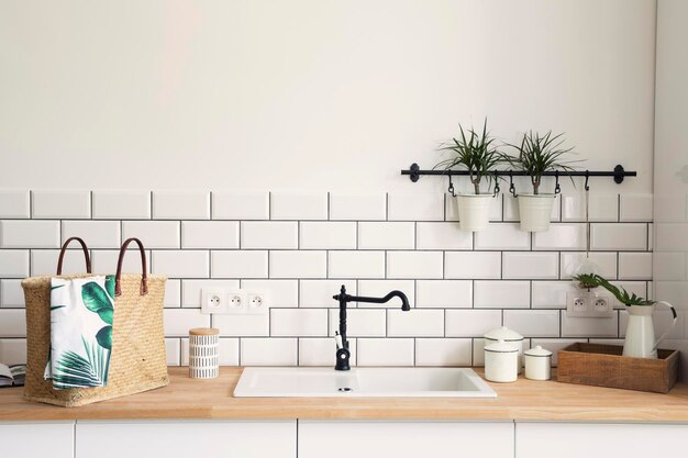 Stylish details of creative kitchen interior in scandinavian apartment with black tap basket tiny plants and other accessoires White creative wall wooden furniture