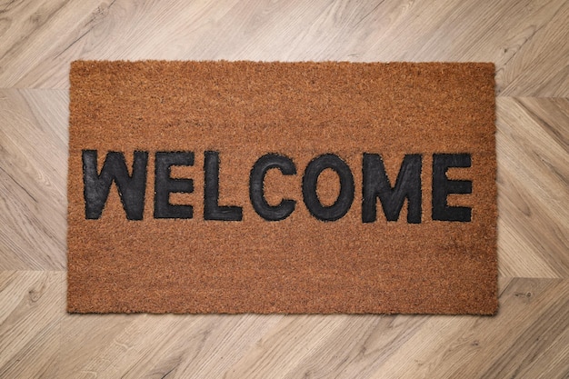 Stylish door mat with word Welcome on wooden floor top view