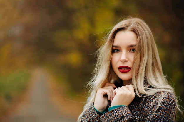 Stylish dressed lovely woman with long hair posing at the autumn street. Space for text