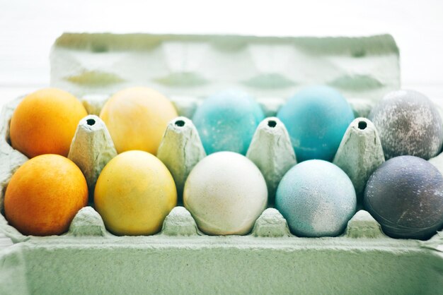 Stylish Easter eggs in carton tray on white wooden background space for text Modern colorful easter eggs painted with pastel natural dye in rainbow colors Happy Easter Holiday decor