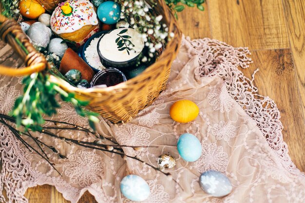 Stylish Easter eggs easter bread cake ham beets sausage butter green branches in wicker basket on rustic fabric with spring flowers Happy Easter holiday traditional feast