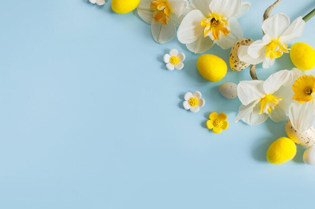 Stylish Easter eggs and yellow daffodils flowers flat lay on blue background with copy space Happy Easter Greeting card template Modern holiday banner Festive composition