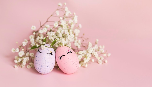 Stylish Easter pink and liliac eggs with cute faces in floral wreath crowns pink background Happy Easter concept Copy space Isolated