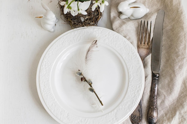Stylish Easter table setting flat lay Pussy willow branch feather on modern plate