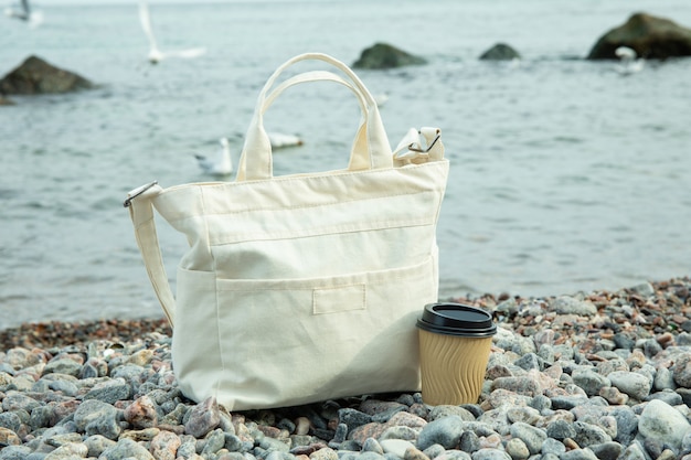 Photo stylish eco bag and paper cup outdoor on sea shore