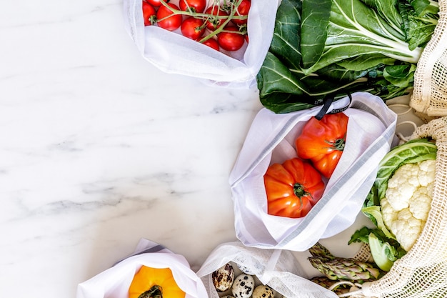 Stylish eco concept on the marble table with zero waste bags, nuts, seeds, eggs, herbs, bio vegetables and fresh fruits. Taking care of earth. Stop plastic. Copy space.