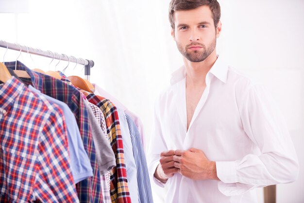 Stile ed eleganza. bel giovane che si veste con una camicia bianca e guarda la telecamera