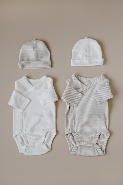 Фото Стильные элегантные базовые боди и шапочки для новорожденных на нейтральном пастельно-бежевом фоне плоский вид сверху