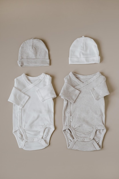 Stylish elegant newborn baby basic bodysuits and hats on neutral pastel beige background Flat lay top view