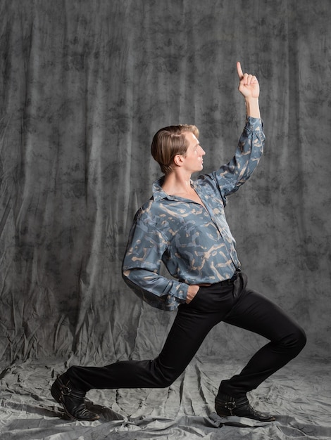 Foto elegante giovane uomo elegante in una camicia di seta blu in posa in studio su uno sfondo di tessuto grigio supe