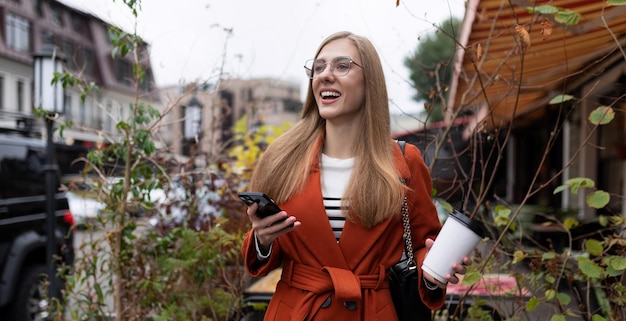 Stylish emotional beautiful girl with a phone and a glass of coffee on the background of a city cafe