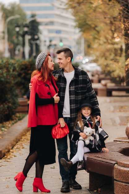 A stylish family of three strolls through the autumn city posing for a photographer Dad mom and daughter in the autumn city