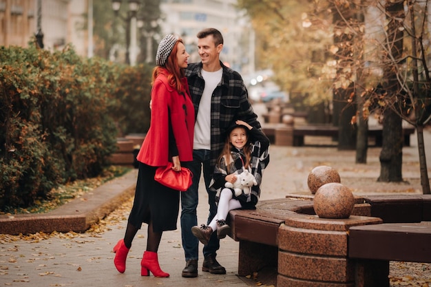 세련된 3인 가족이 가을 도시에서 사진작가 아빠 엄마와 딸을 위해 포즈를 취하며 가을 도시를 산책합니다.