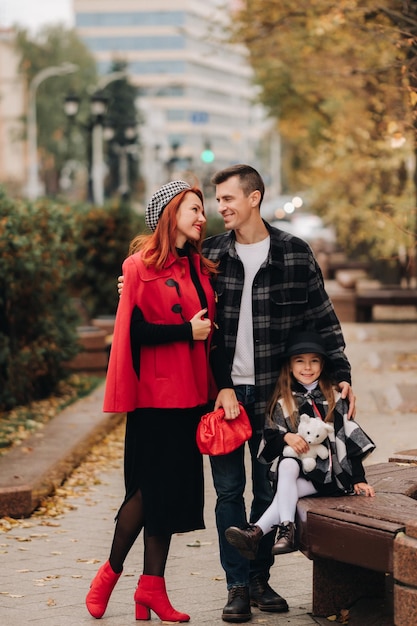 A stylish family of three strolls through the autumn city\
posing for a photographer dad mom and daughter in the autumn\
city