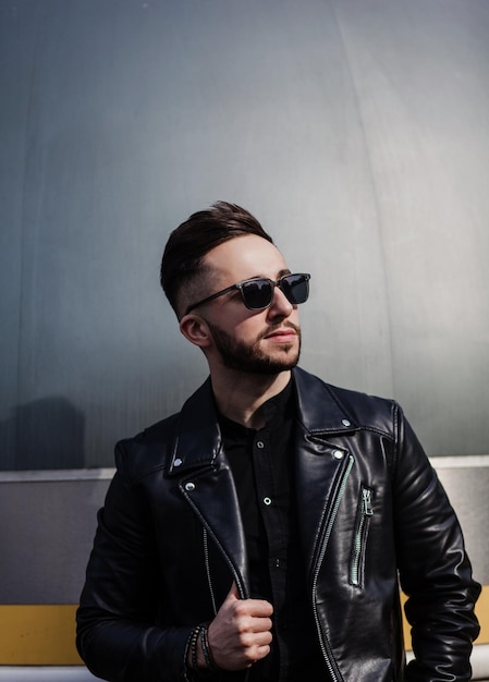 stylish fashion man posing in sunglasses and black leather jacket