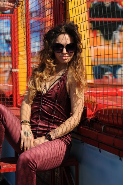 Stylish fashion woman portrait, dressed in dark red velor overalls, outdoors in amusement park