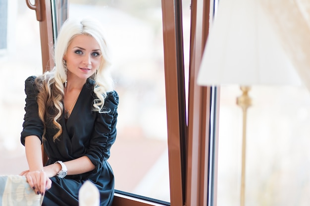 Elegante donna bionda alla moda con il trucco in guarisce giacca nera sul balcone della città concetto di moda primavera autunno rumore di arte morbida messa a fuoco selettiva