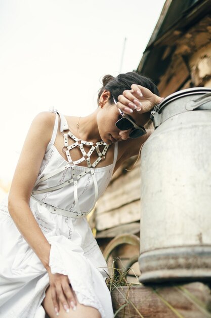 Stylish female farmer rests near milk can after work Outdoor shot