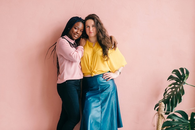 Stylish female interracial couple hugging on pink background.