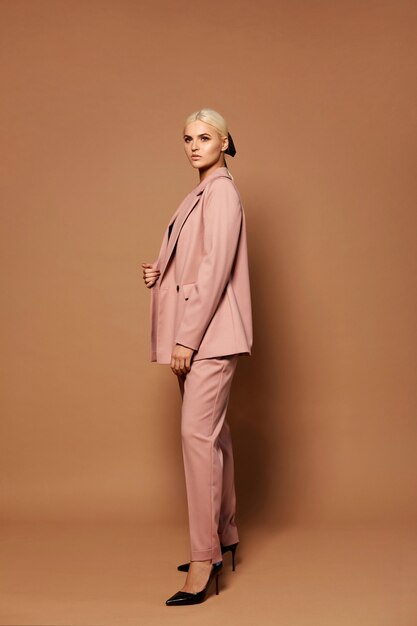 Stylish female model with blond hair in trendy pink suit and shoes posing on a beige background studio shot of a young woman in official style clothes