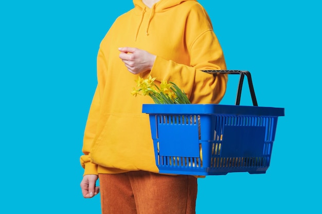 Photo stylish female in yellow hoodie with blue basket and flowers on blue background