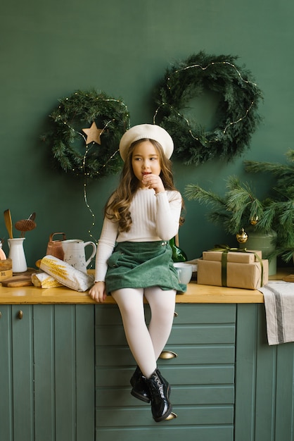 Stylish girl in a beret sitting in the kitchen, decorated for Christmas and New Year and eating baguette